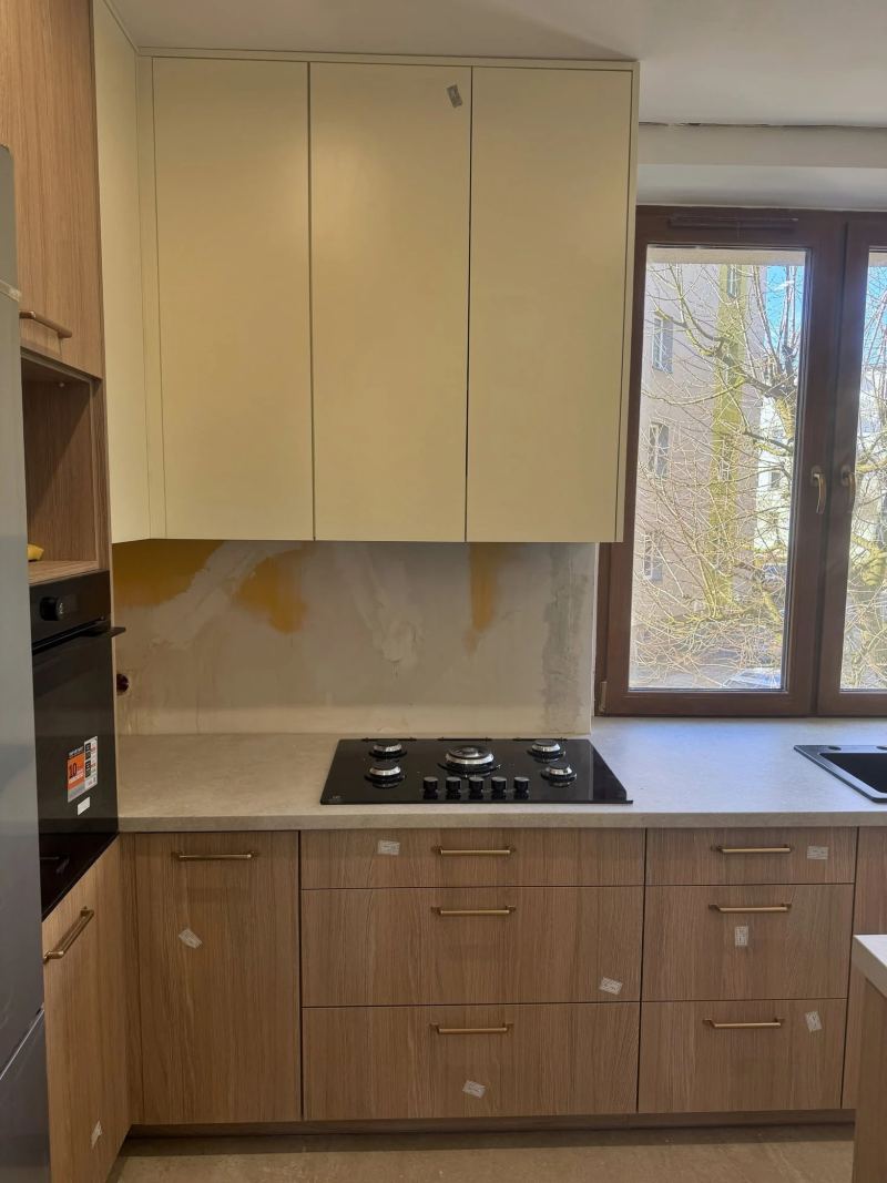 Kuchnia z frontami dolnymi w dekorze drewna, złotymi uchwytami i kremową zabudową górną nad płytą gazową